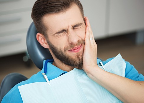 Man in dental chair holding jaw