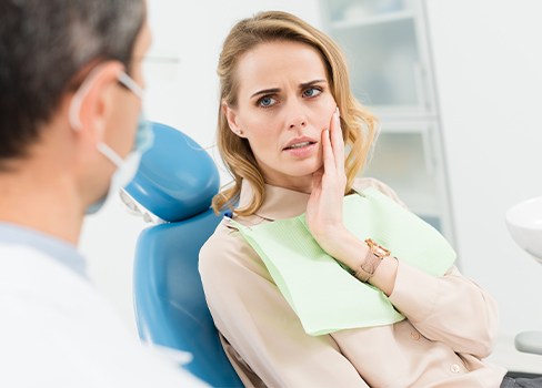 Woman in dental chair holding jaw